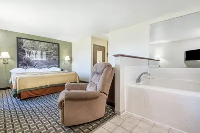 a hotel room with a bed and a chair and a tub at Super 8 by Wyndham Madison IN in Madison