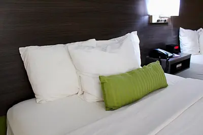 a white bed with white pillows and a green pillow at Baymont by Wyndham Springfield in Springfield