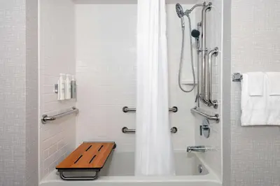 a bathroom with a shower and a tub with a wooden bench at Hampton Inn & Suites Cleveland-Beachwood in Beachwood