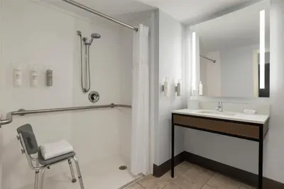 a bathroom with a sink and a shower and a chair at Hilton Garden Inn Cleveland Airport in Fairview Park
