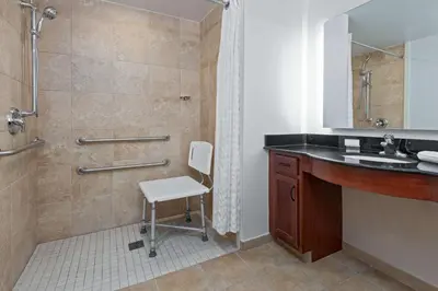 a bathroom with a shower and a sink and a chair at Homewood Suites by Hilton Cleveland-Beachwood in Beachwood