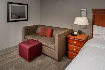 a hotel room with a couch with a red pillow and a bed at Hampton Inn Charleston Downtown in Charleston