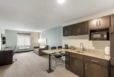 an apartment kitchen with a counter and a living room at MainStay Suites Logan Ohio-Hocking Hills in Logan