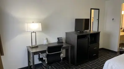 a hotel room with a desk with a lamp and a television at La Quinta Inn and Suites by Wyndham Cincinnati North in Springdale