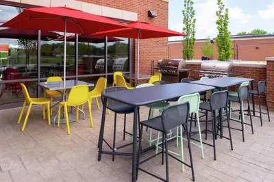 a group of tables and chairs with umbrellas on a patio at Home2 Suites By Hilton New Albany Columbus in New Albany