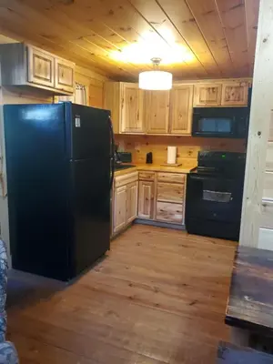 a kitchen with a black refrigerator and wooden cabinets at The Frontier - An Amish Built Deluxe Cabin in Genoa