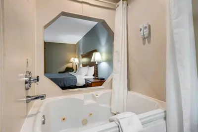 a bathroom with a tub and a bed and a mirror at Quality Inn & Suites Near Amish Country in Rushville