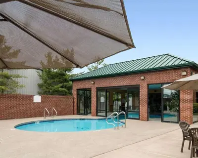 a building with a swimming pool in front of a house at Comfort Suites Parkersburg South in Mineralwells