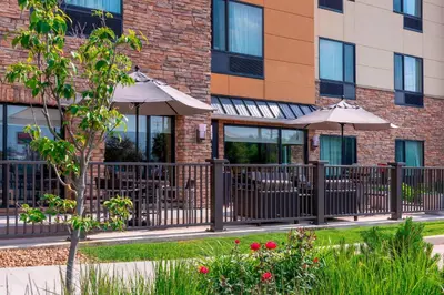 a building with tables and umbrellas in a courtyard at TownePlace Suites Fort Wayne North in Fort Wayne