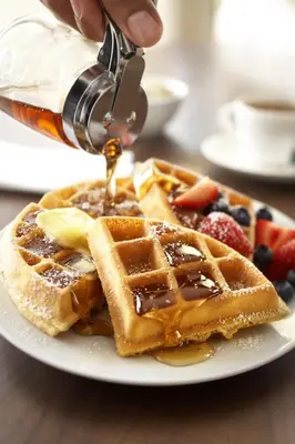 a person is pouring syrup onto a plate of waffles at Country Inn & Suites by Radisson, Marion, OH in Marion