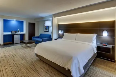a hotel room with a large bed and a blue chair at Holiday Inn Express & Suites Troy by IHG in Troy
