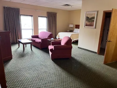a hotel room with a bed and a couch and chairs at Days Inn & Suites by Wyndham Sutton Flatwoods in Sutton
