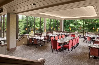 a restaurant with tables and red chairs and windows at Sheraton Suites Akron Cuyahoga Falls in Cuyahoga Falls
