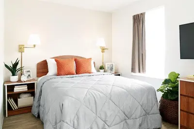 a white bedroom with a bed with orange pillows at InTown Suites Extended Stay Columbus OH - I-70E Hamilton Rd in Columbus