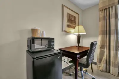 a room with a desk with a microwave and a table with a chair at Baymont by Wyndham Zanesville in Zanesville