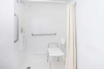a white shower with a white chair in a bathroom at Super 8 by Wyndham Newcomerstown in Newcomerstown