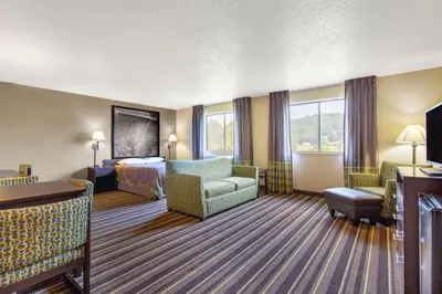 a hotel room with a bedroom and a bed and a couch at Super 8 by Wyndham Weston WV in Weston