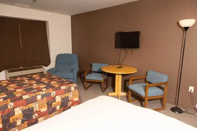 a room with a bed and chairs and a table and a tv at Lafayette Inn in Moundsville