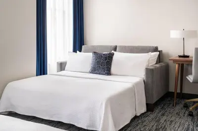 a bed with white sheets and pillows next to a couch at BLU-Tique, Akron, a Tribute Portfolio Hotel in Akron