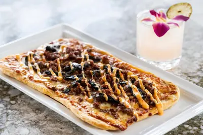 a plate with a pizza on a table with a drink at BLU-Tique, Akron, a Tribute Portfolio Hotel in Akron
