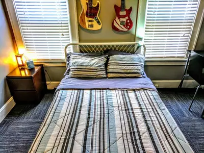 a bed in a room with a guitar on the wall at The Wayfaring Buckeye Hostel in Columbus