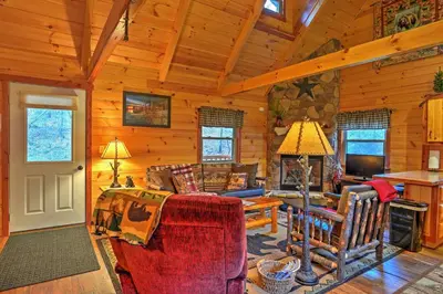 a living room with a couch and a fireplace at Rustic Dundee Log Cabin with Hot Tub and Forest Views! in Dundee