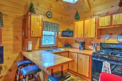 a kitchen with wooden cabinets and a stove at Rustic Dundee Log Cabin with Hot Tub and Forest Views! in Dundee