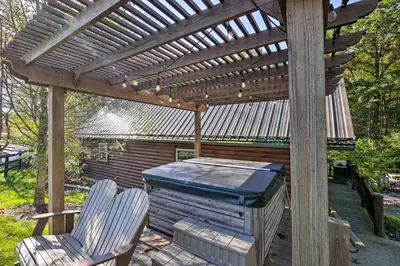 a wooden pergola with two chairs and a grill at Rustic Dundee Log Cabin with Hot Tub and Forest Views! in Dundee