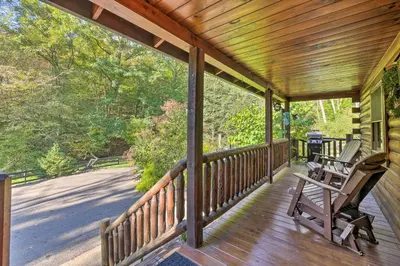 a porch with two rocking chairs on it at Rustic Dundee Log Cabin with Hot Tub and Forest Views! in Dundee