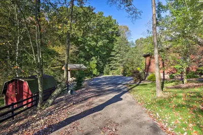 a road in the woods with a fence and a cabin at Rustic Dundee Log Cabin with Hot Tub and Forest Views! in Dundee