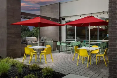 a patio with tables and yellow chairs and red umbrellas at Home2 Suites By Hilton Marysville in Marysville
