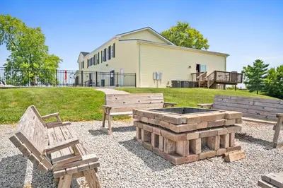 a fire pit and two benches in front of a building at Country Lodge for 18, With Pool and Pond, Near Ark in Williamstown