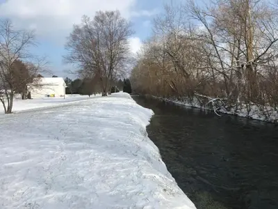 a snow covered path next to a river with trees at Millsite Lodge in Sandusky
