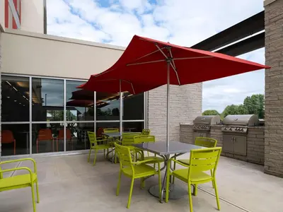 a patio with yellow chairs and a table with a red umbrella at Home2 Suites Troy, OH in Troy