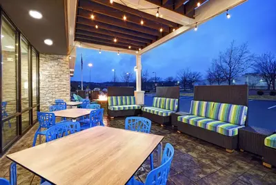 a patio with wooden tables and blue chairs at Home2 Suites By Hilton Springdale Cincinnati in Springdale