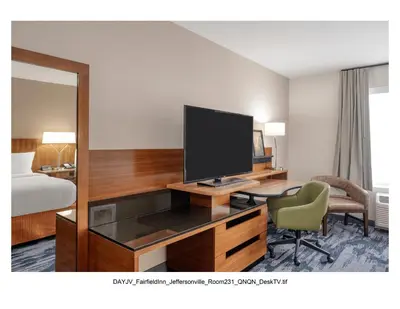 a hotel room with a desk with a television and a bedroom at Fairfield Inn & Suites by Marriott Jeffersonville I-71 in Jeffersonville