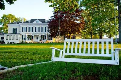 a white bench in front of a white house at Riverside Inn Bed and Breakfast, Wedding Venue & Events in Warsaw