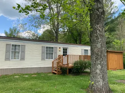 a mobile home with a deck and a tree at Convenient and Spacious home in Stanton, Ky in Stanton