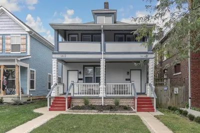 a blue house with a white porch and a brick building at Chic 2BR near DT, 8 min walk to Park&Conservatory in Columbus