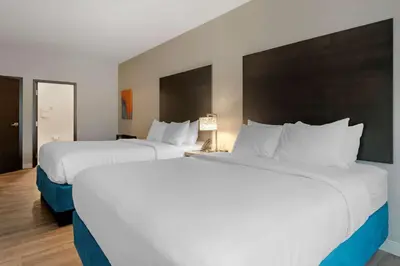 two beds in a hotel room with white sheets at MainStay Suites Cincinnati University - Uptown in Cincinnati