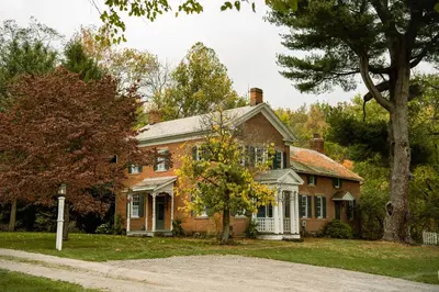 a brick house with a tree in front of it at Timeless Winesburg Farmhouse with Deck in Dundee