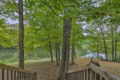 a wooden bench in a park with trees and a lake at Rustic Cabin in the Woods 2-Acre Fishing Pond! in Burlington