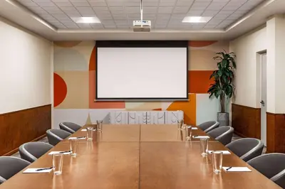 a conference room with a table and a white screen at The Orbit Hotel, Trademark Collection by Wyndham in Fairview Park