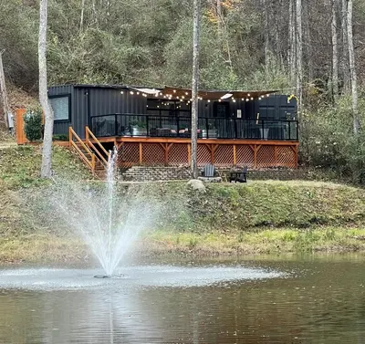 a house sitting on the side of a pond with a fountain at The Hideaway on Tacketts - Shipping Container in Hurricane