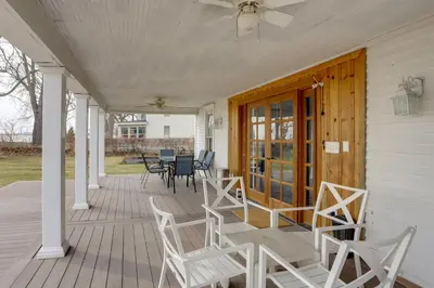 a porch with white chairs and a ceiling fan at Spacious Lakefront House with Backyard Fire Pit in Monroe