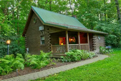 a log cabin with a porch and a green roof at Apple Blossom Cabin by Amish Country Lodging in Millersburg