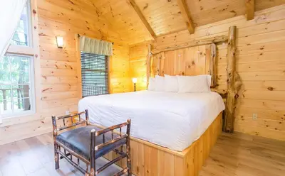 a bedroom with a bed and a chair in a log cabin at Lofty Willows Treehouse by Amish Country Lodging in Millersburg