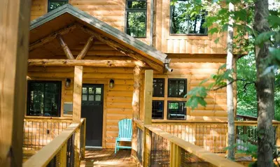 a log cabin with a front porch and a blue chair at Treehouse #2 by Amish Country Lodging in Millersburg