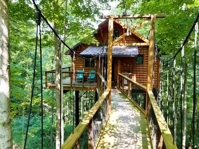 a tree house in the forest with a suspended walkway at Treehouse #4 by Amish Country Lodging in Millersburg