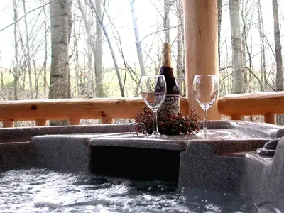 two wine glasses on a hot tub with a bottle of wine at Wild Rose Cabin by Amish Country Lodging in Millersburg
